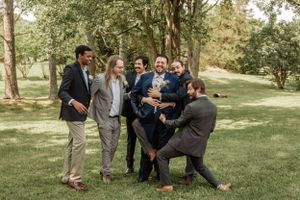 Wedding party members engaged in candid fun moment on sunny lawn.
