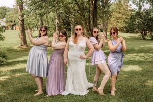 Bridesmaids in flowing pastel dresses gather for casual photos on grass.