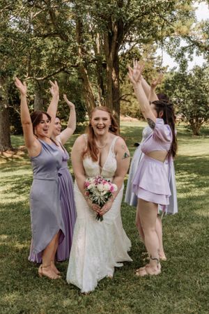 Wedding party members raise arms in joyful celebration outdoors.