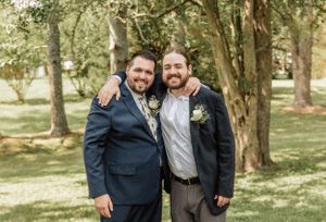 Groomsmen in suits pose for candid photos in a natural outdoor setting with trees in the background.