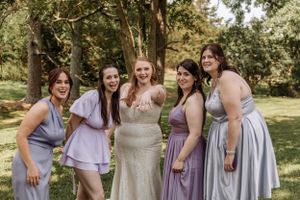 Wedding party stands together outdoors in coordinating purple and gray dresses with bouquets.
