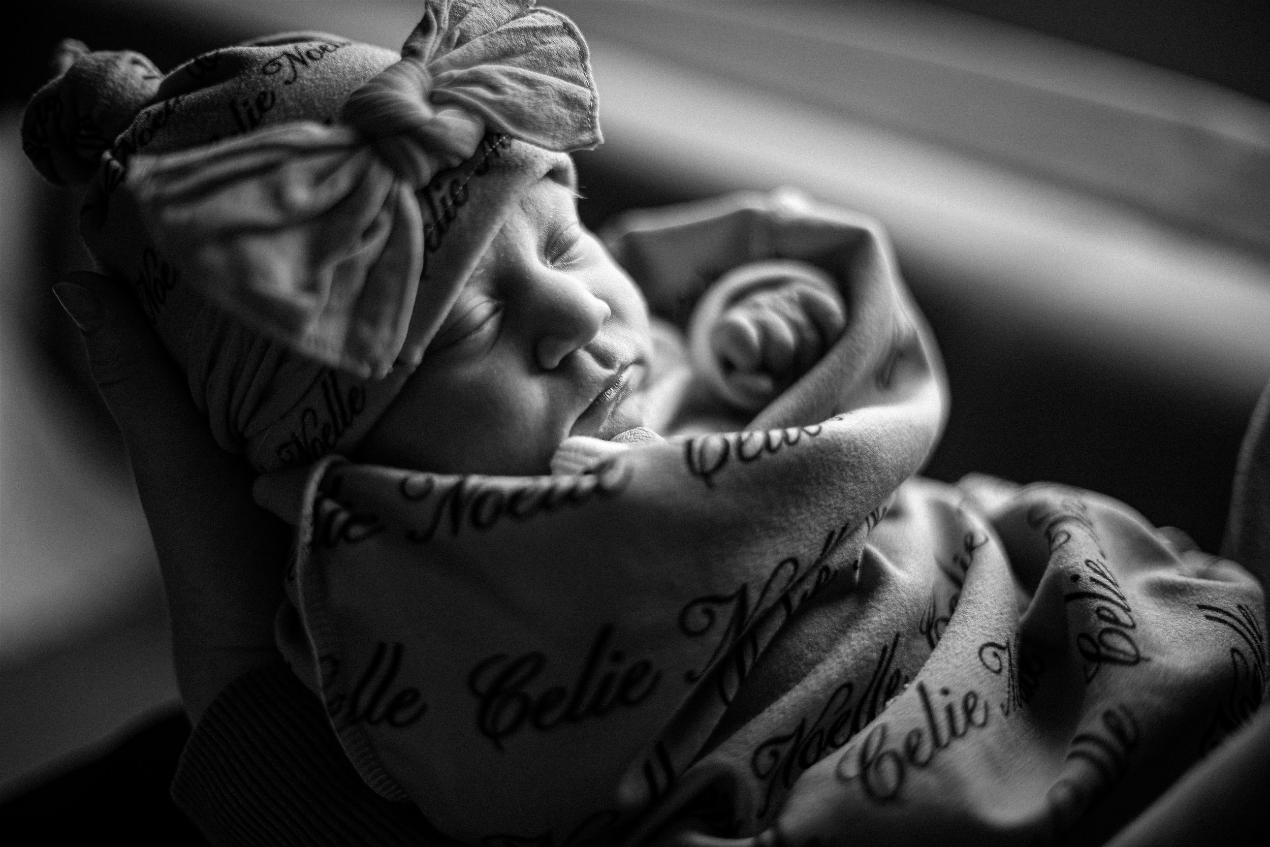 Black and white artistic portrait of sleeping infant wrapped in patterned blanket.