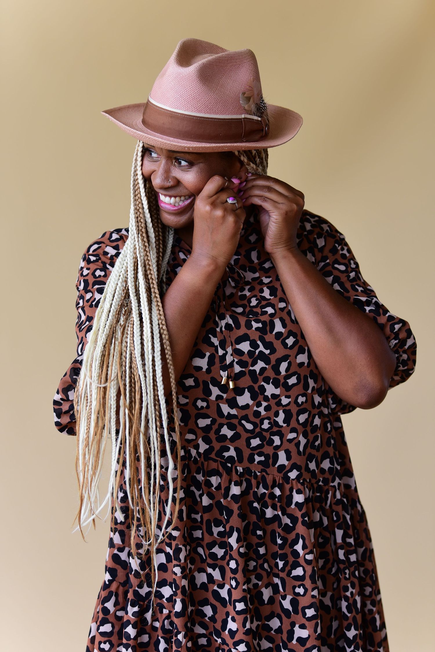 Playful portrait featuring a brown fedora and patterned dress with long blonde braids.
