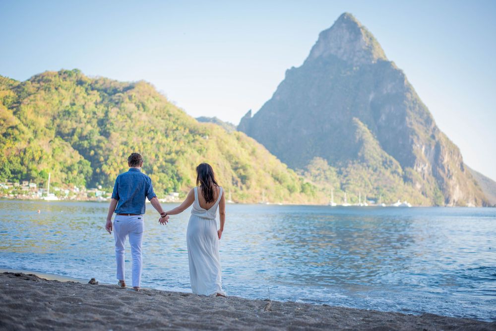 Couple strolling along tropical beach with majestic Pitons mountains in background.
