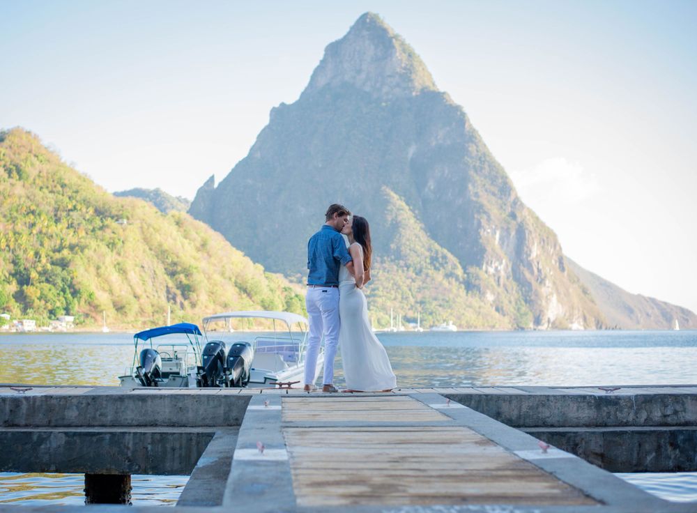 A couple stands on a wooden pier with the iconic Pitons mountains of St Lucia in the background.