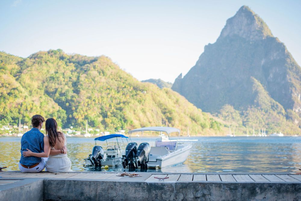 A couple sits on a dock overlooking the majestic Pitons mountains and Caribbean waters.
