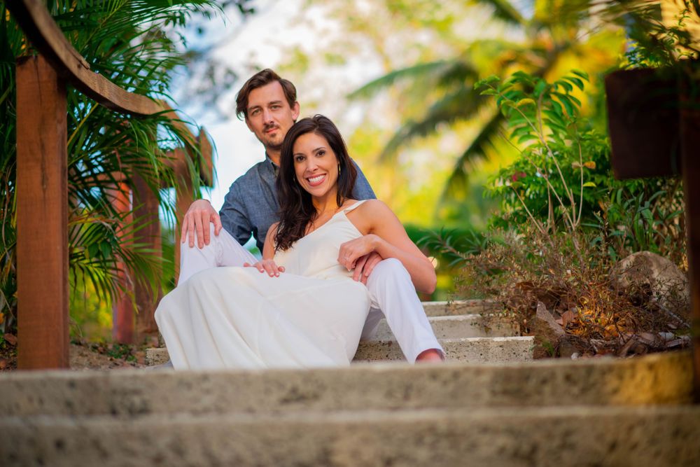 A couple poses on tropical stone steps surrounded by lush palm trees.