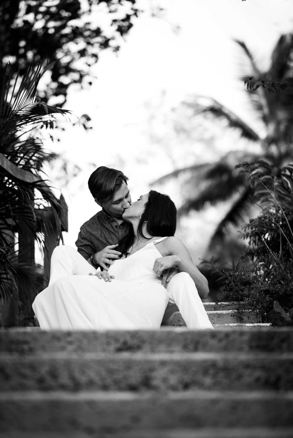 A black and white romantic portrait on stone steps with palm trees in the background.