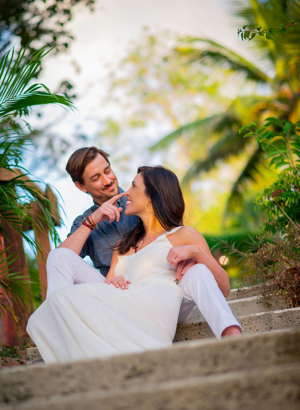 A tender moment captured on tropical stone steps surrounded by palm fronds.
