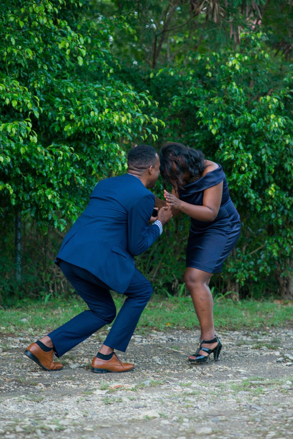 A playful moment between a couple in formal attire against green foliage.