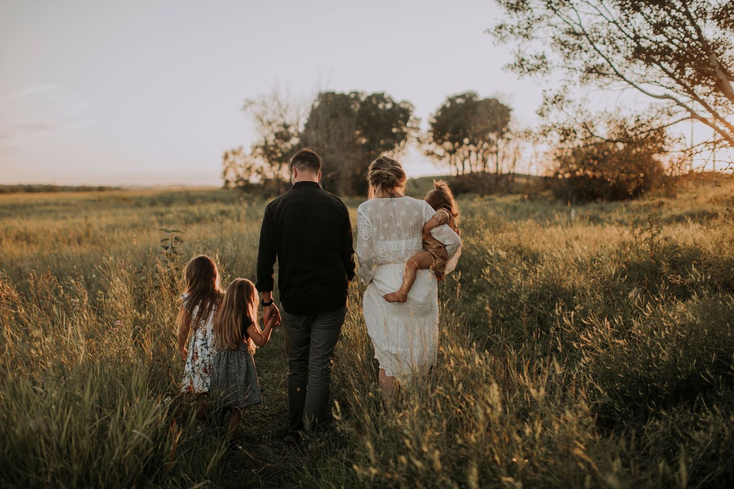 A family walks together through a sun-drenched meadow at golden hour.