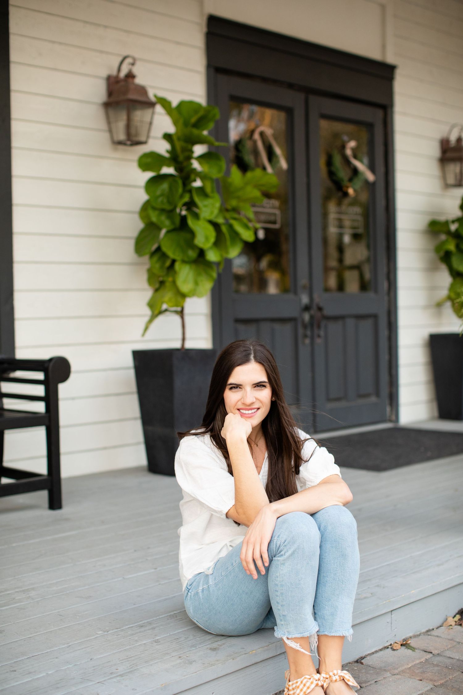 Woman sits casually on gray porch floor near decorative black doors.