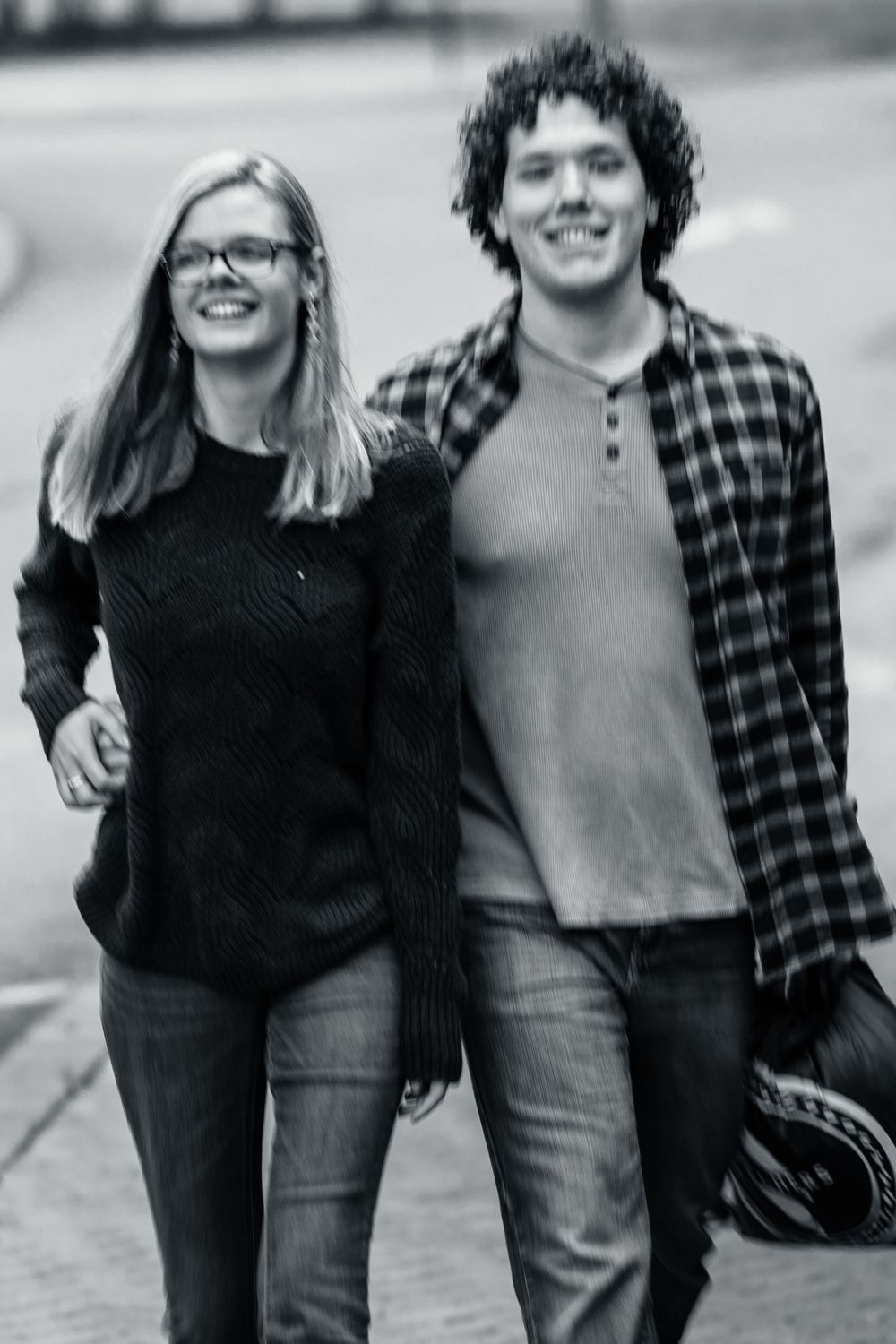 Happy couple walking arm in arm on a street, black and white photo, woman in sweater and man in plaid shirt.