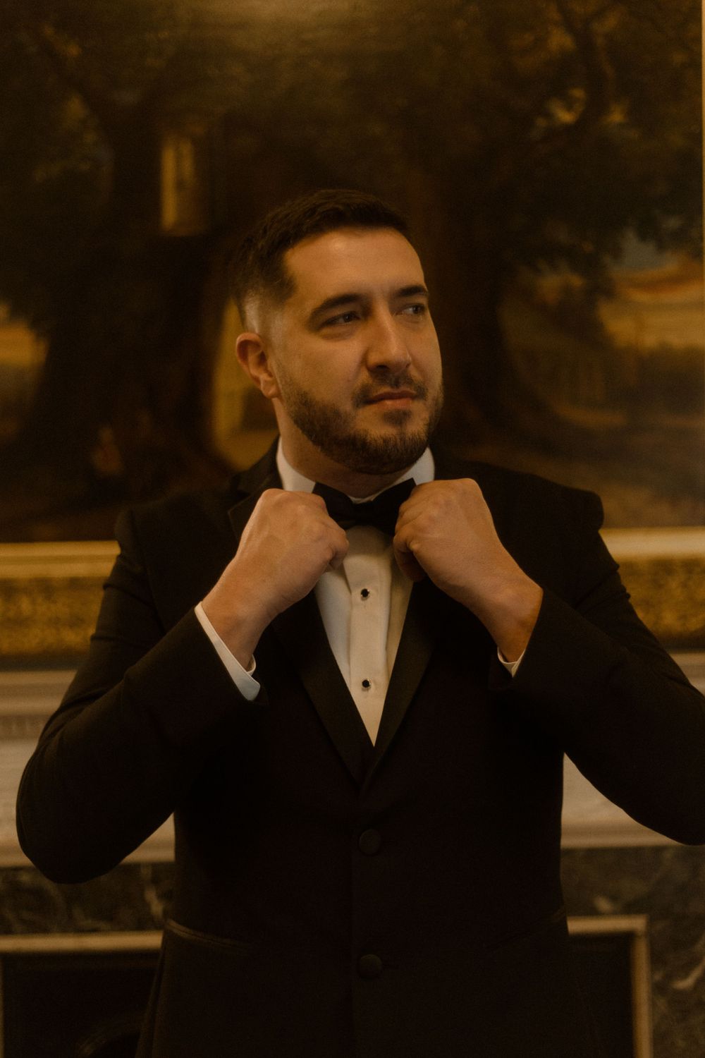 Formal portrait of a person adjusting their bowtie in an elegant gallery setting.