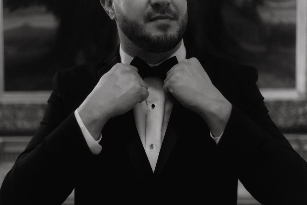 Close-up shot of hands adjusting a black bowtie on a tuxedo.
