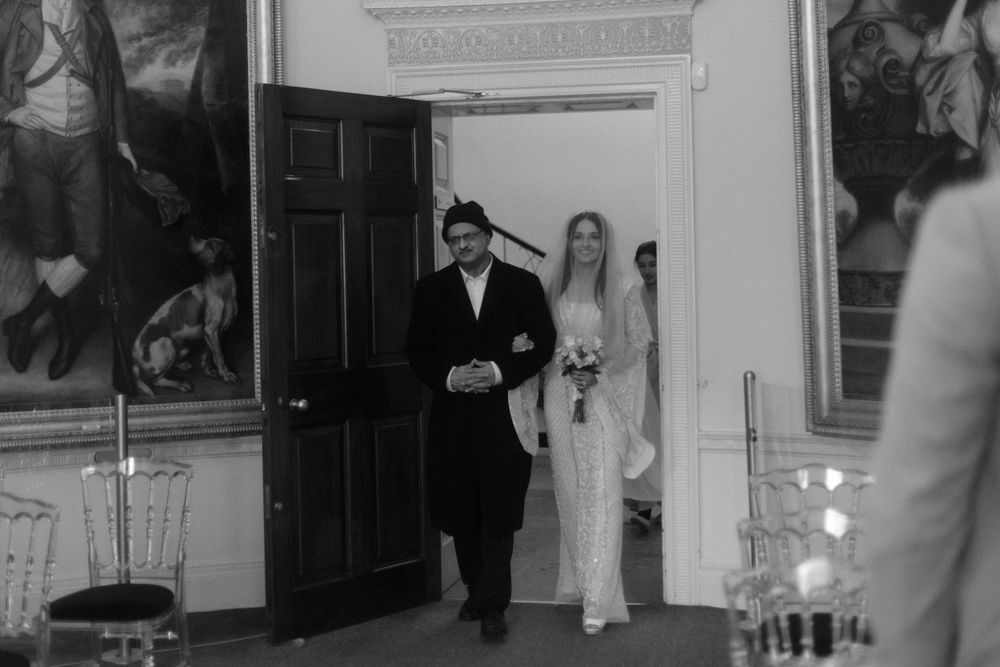 Black and white photo of a wedding ceremony in a historic room with paintings on the walls.