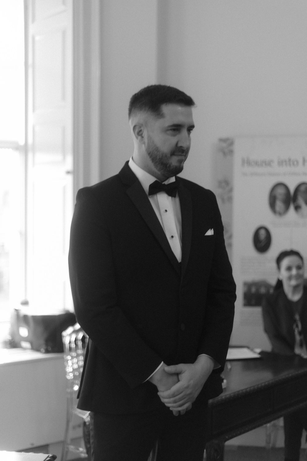 A groom in formal black tuxedo stands in anticipation during wedding ceremony.