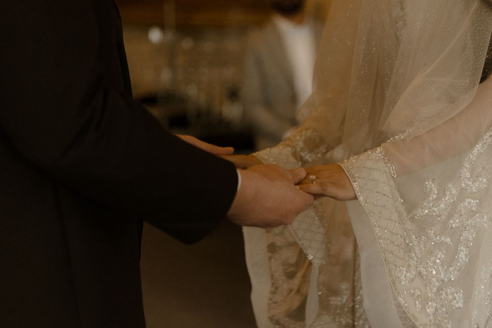 Close-up of couple's hands joined together during wedding ceremony with bride's lace dress visible.