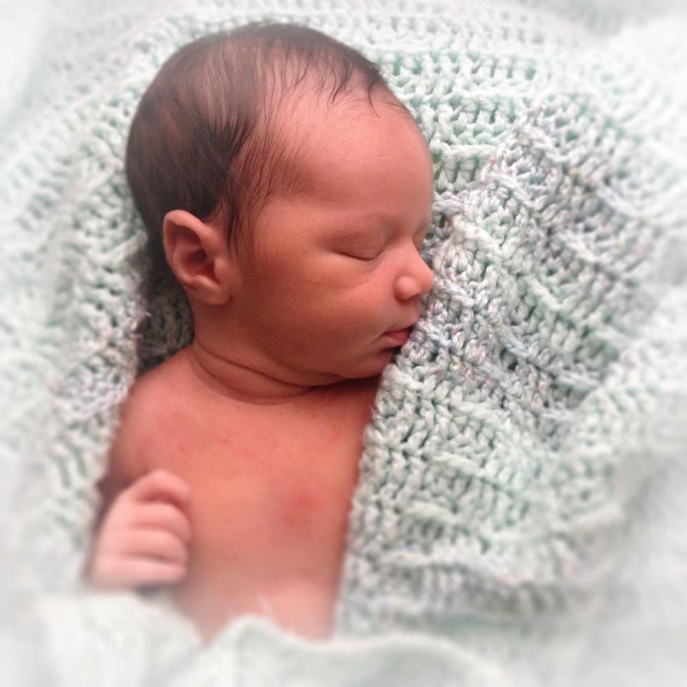 Newborn baby sleeping peacefully wrapped in white knit blanket.