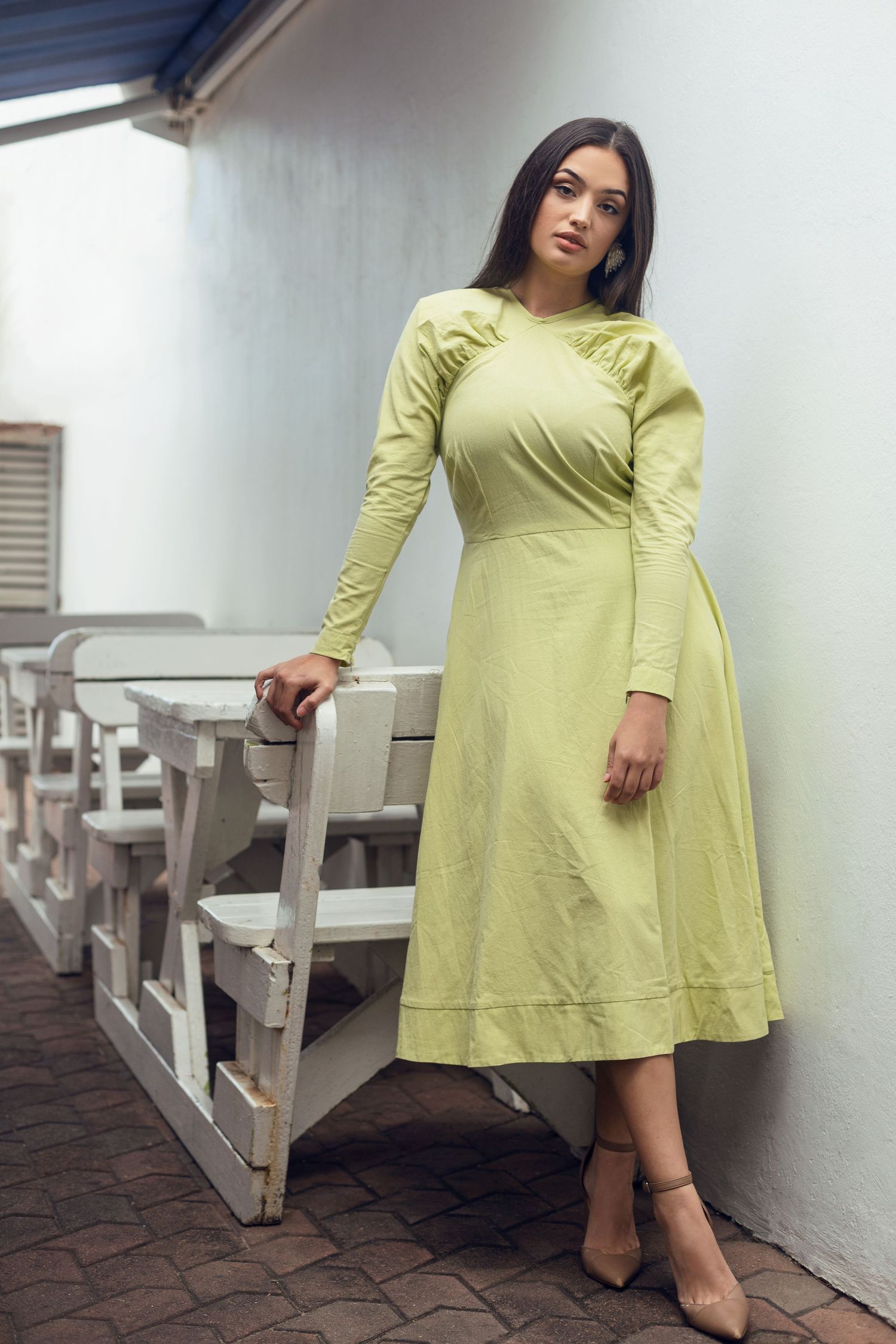 Woman in a lime green vintage-style dress with puff sleeves poses against a white wall.