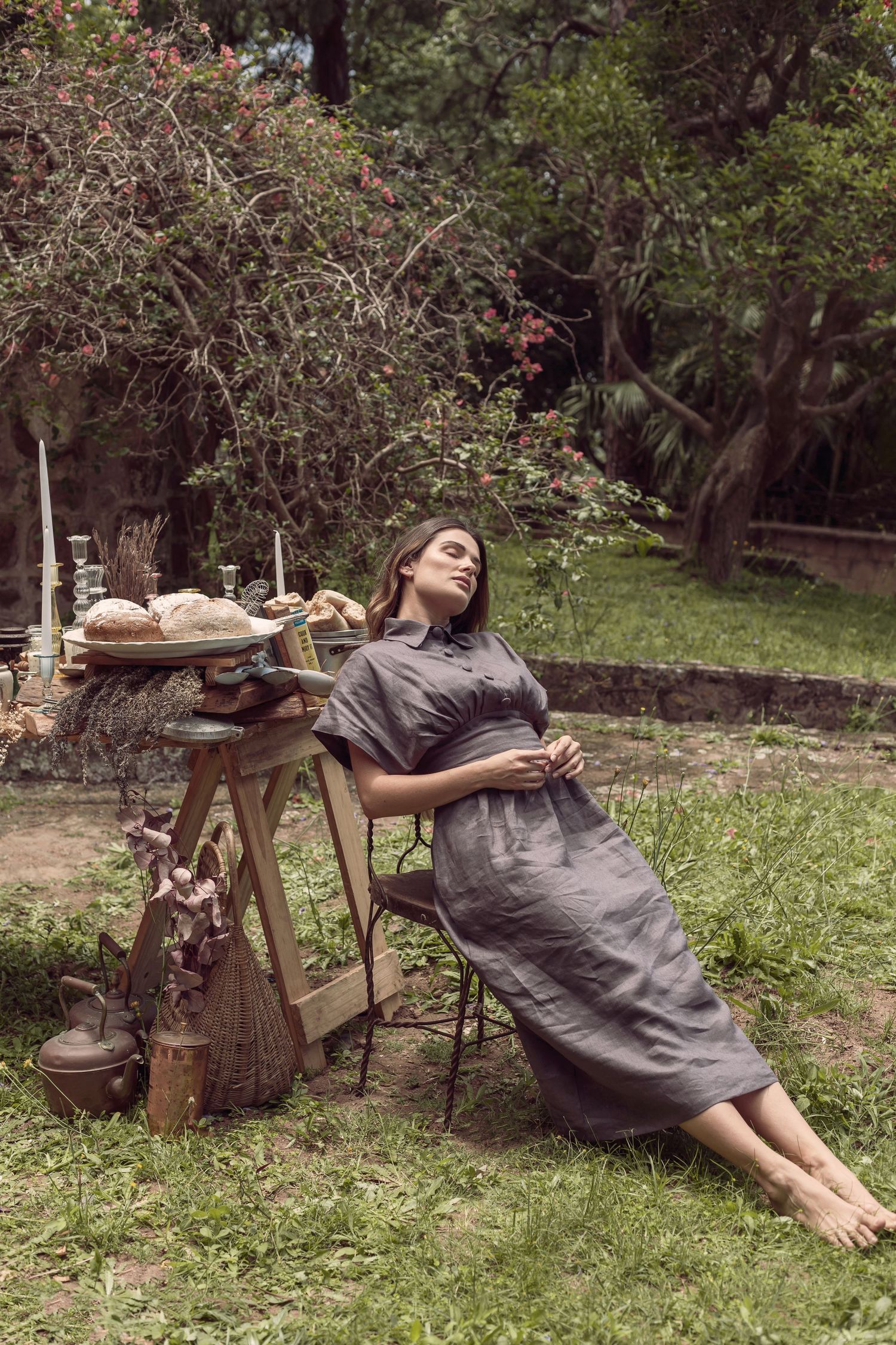 Woman in grey dress relaxing on vintage wooden table in garden setting.