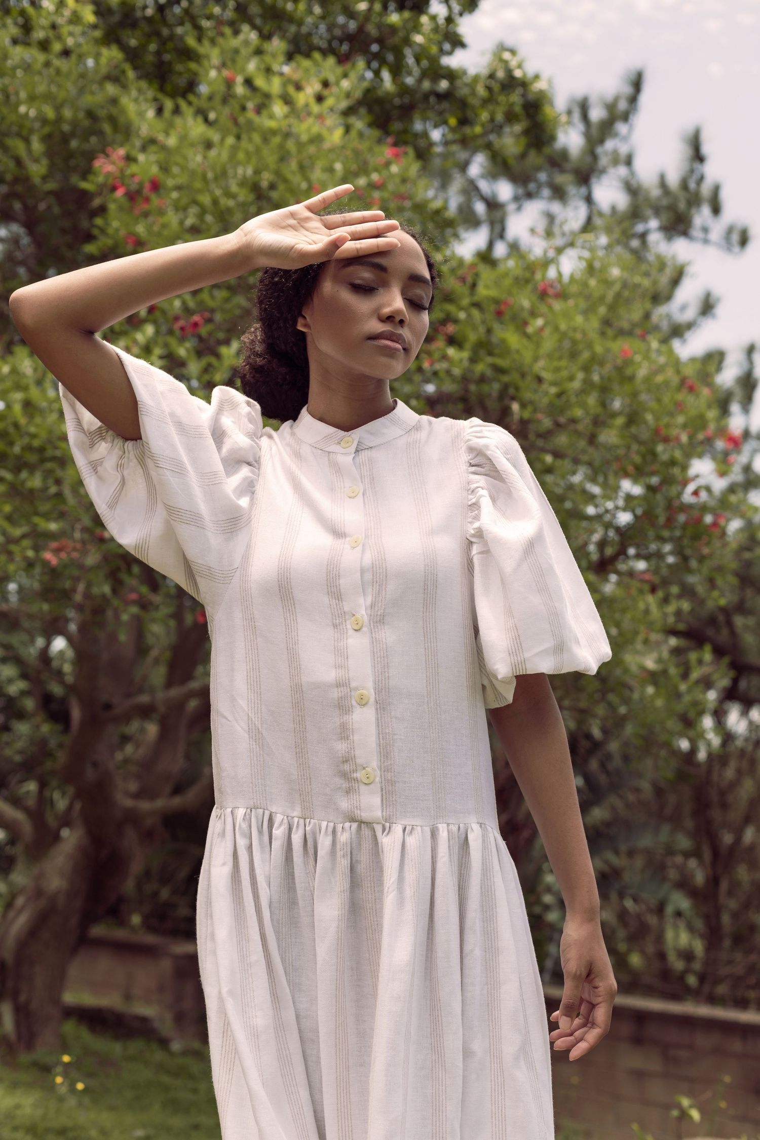 Woman in white cotton dress with puffy sleeves standing in garden setting.