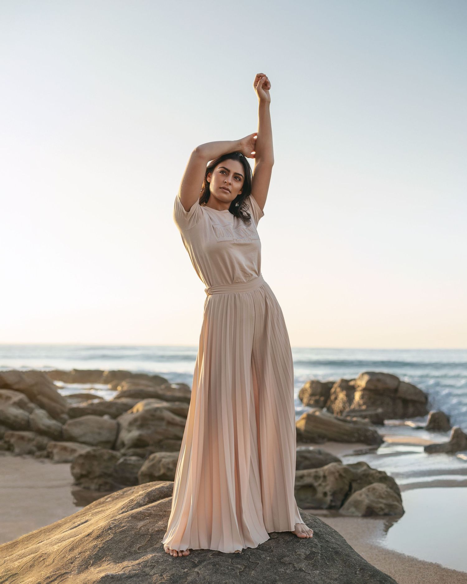 A flowy beige maxi dress captured at sunset on a rocky beach.