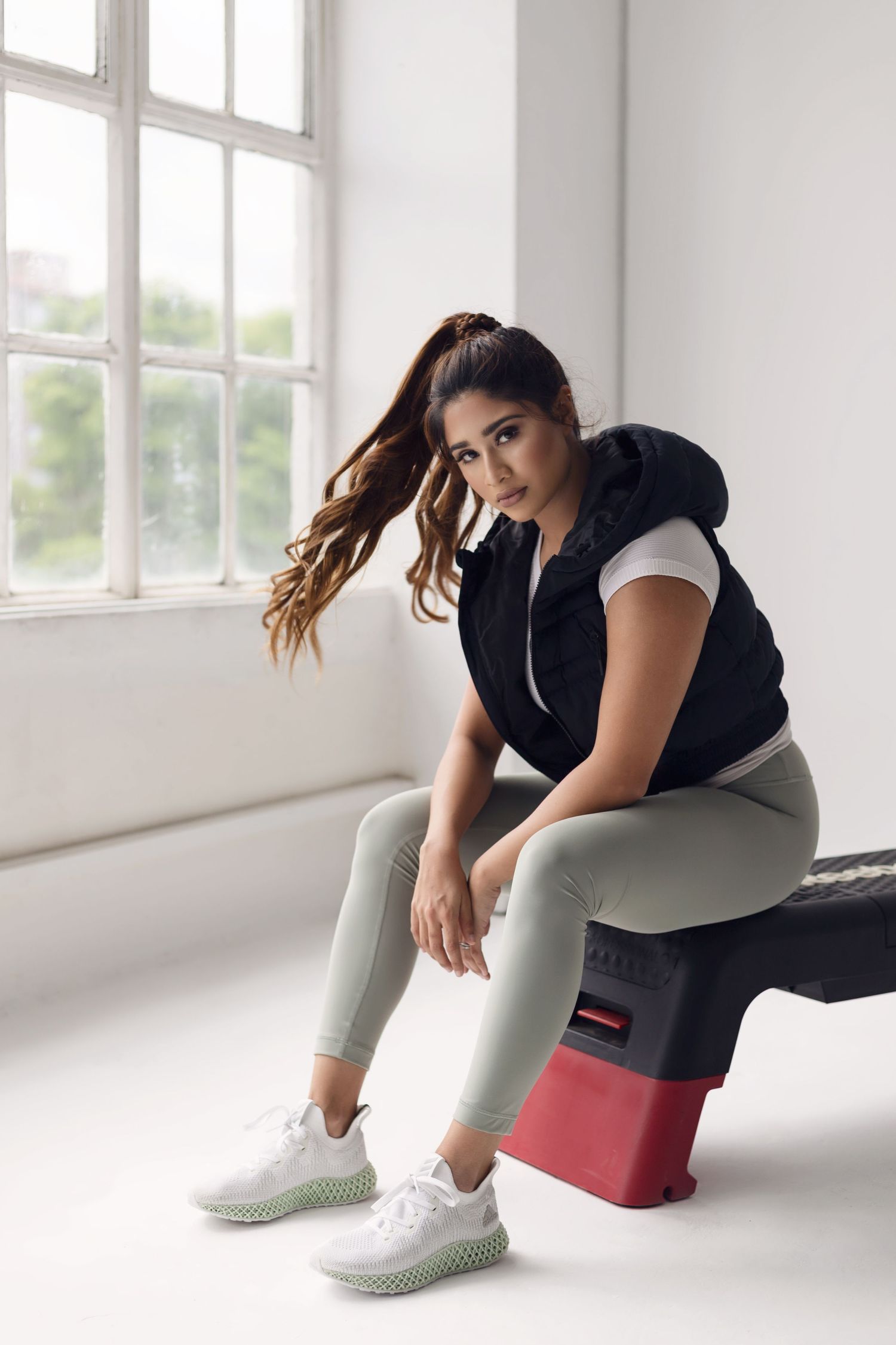 Athletic woman in workout attire sits on exercise equipment in a bright studio setting.