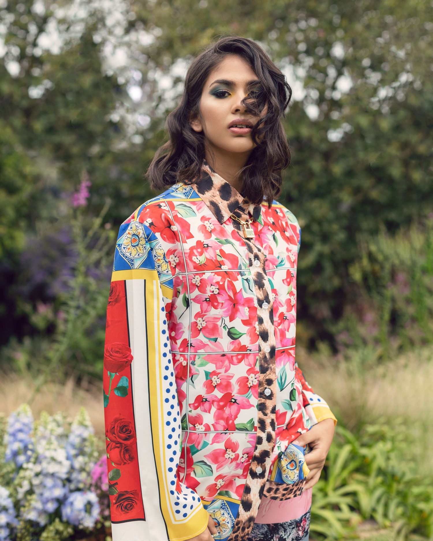 Vibrant floral print shirt with mixed pattern panels photographed in garden setting.