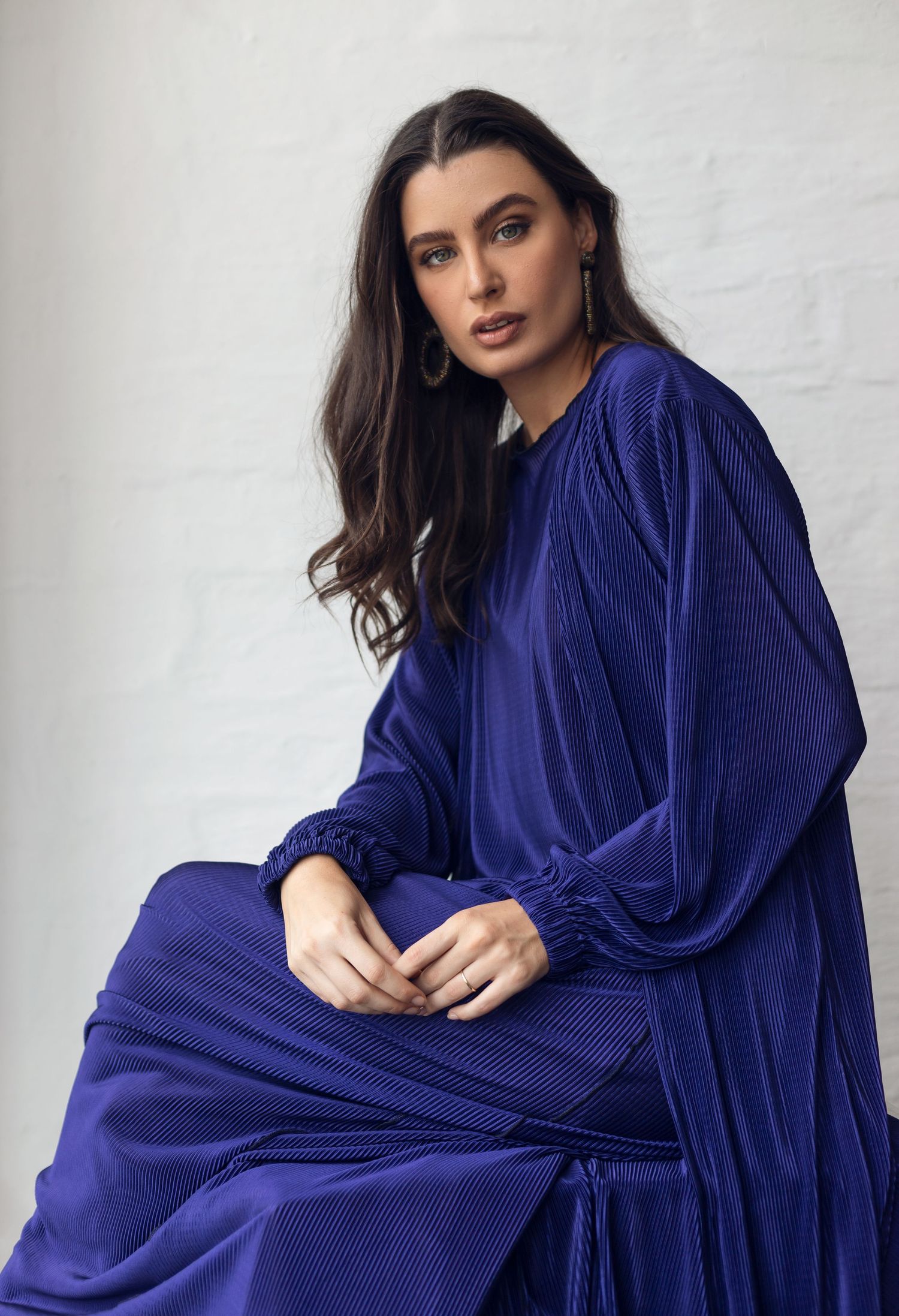 Model in flowing royal blue pleated dress poses against white background.