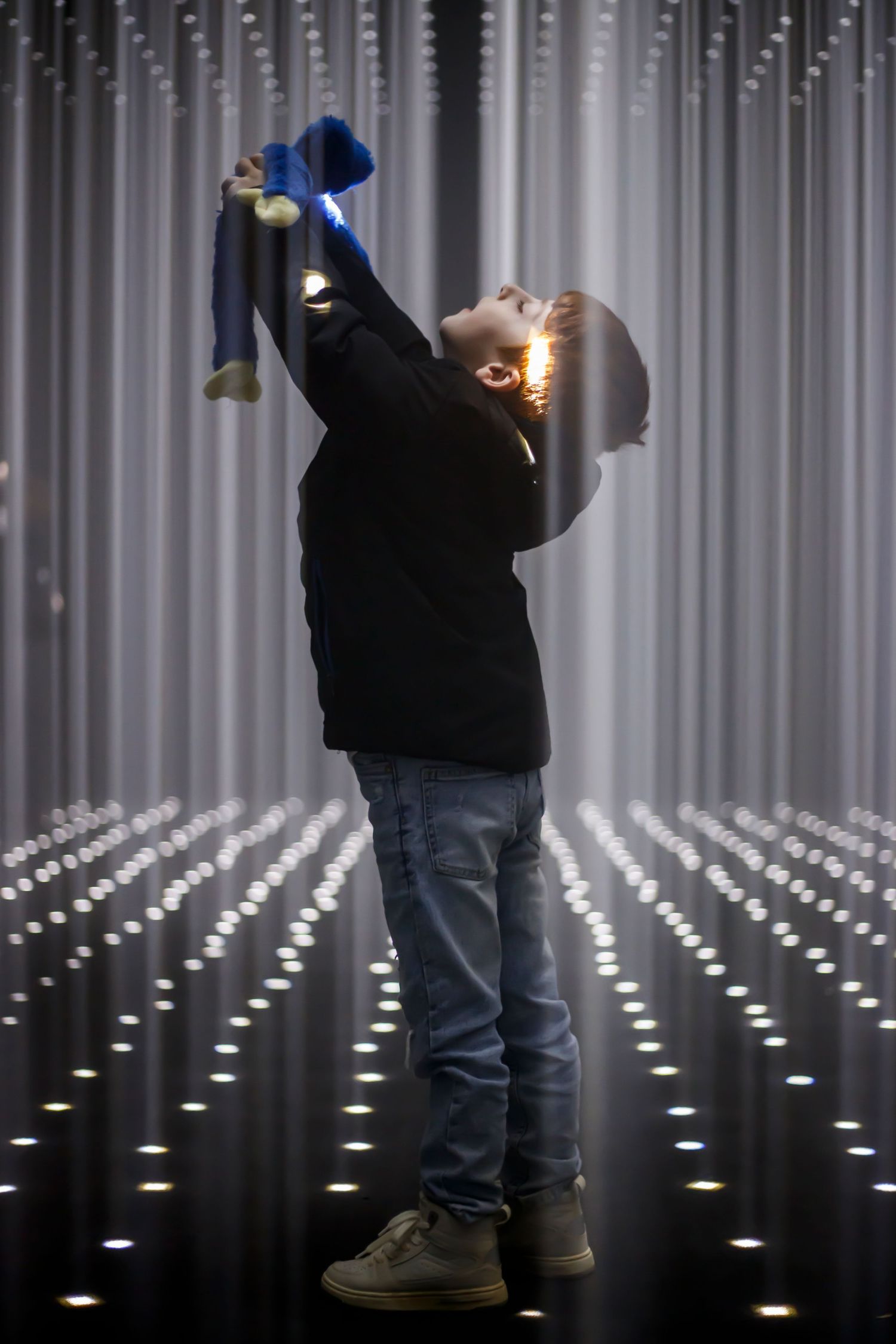 Silhouette against glowing vertical light installation holds toy above while standing in dramatic pose.