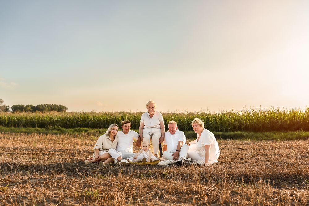 Family dressed in white sits together on ground for sunset portrait near cornfield.
