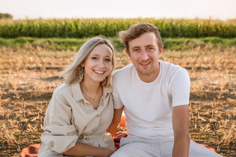 Young couple in casual attire sharing a moment during sunset photoshoot in rural field.