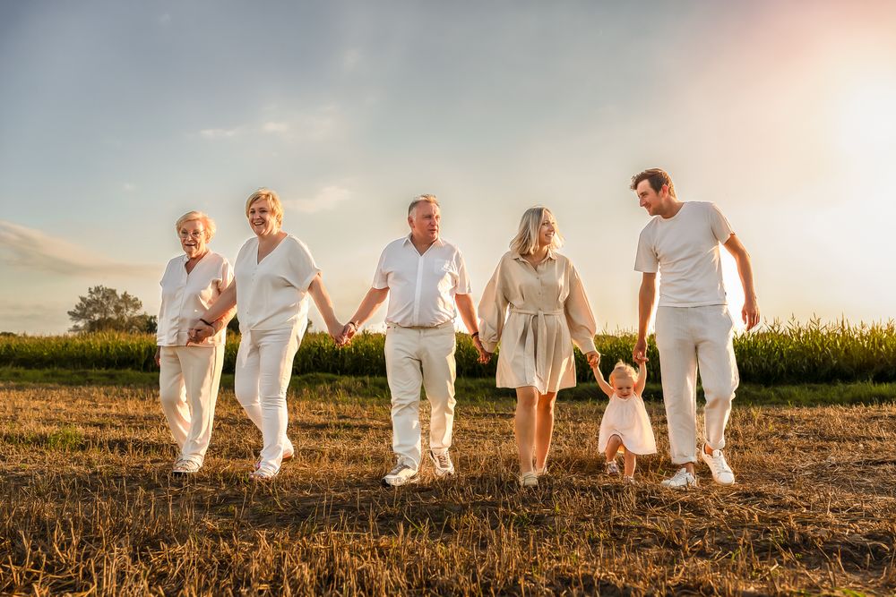 A group walks hand in hand through a sunlit field wearing coordinated white outfits.
