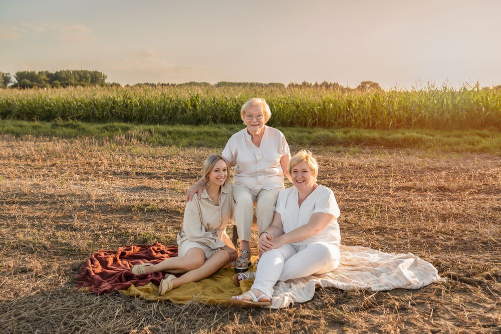 Three people enjoying a picnic on blanket at sunset near cornfield.