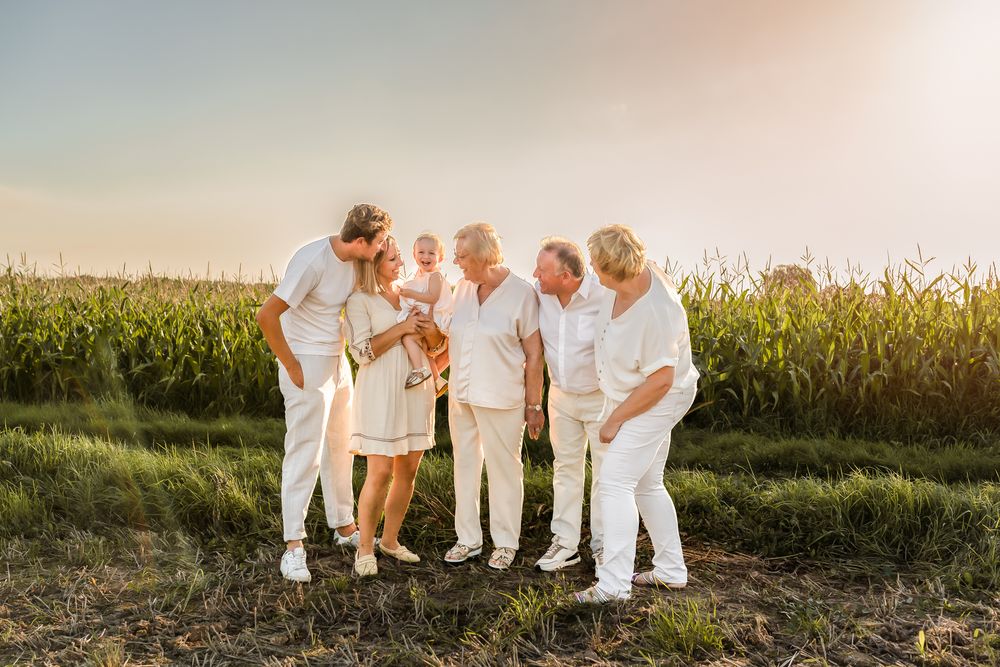 Family gathering in white outfits laughing together at sunset by a cornfield.