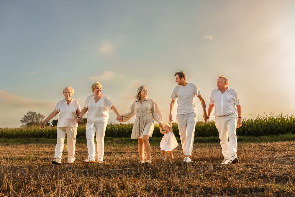 People in coordinated white outfits hold hands while walking through a sunlit field.