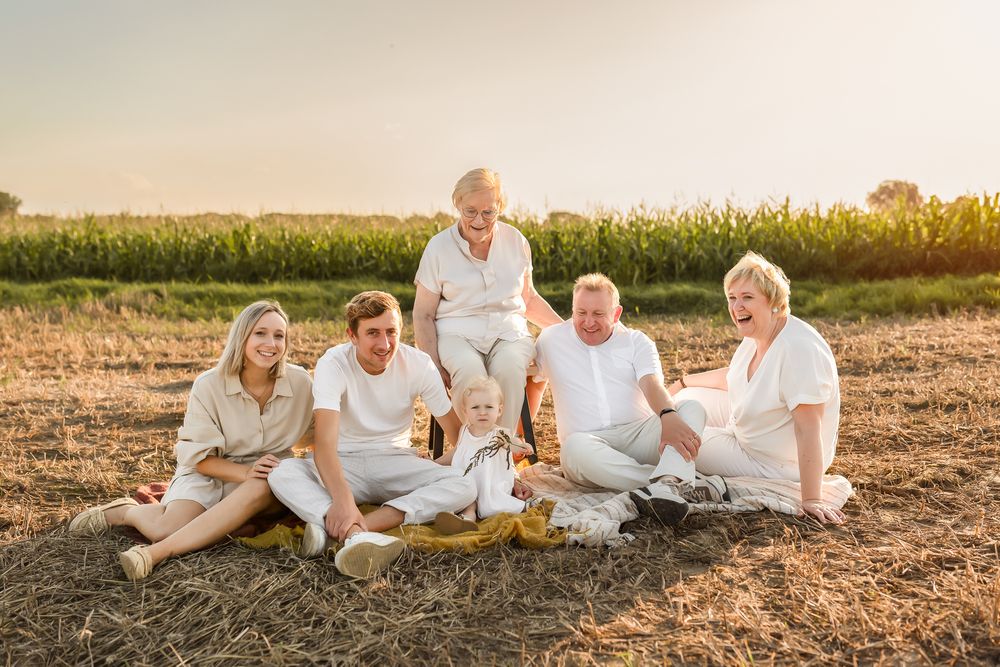 Casual family portrait with everyone in white clothing relaxing on ground at golden hour.