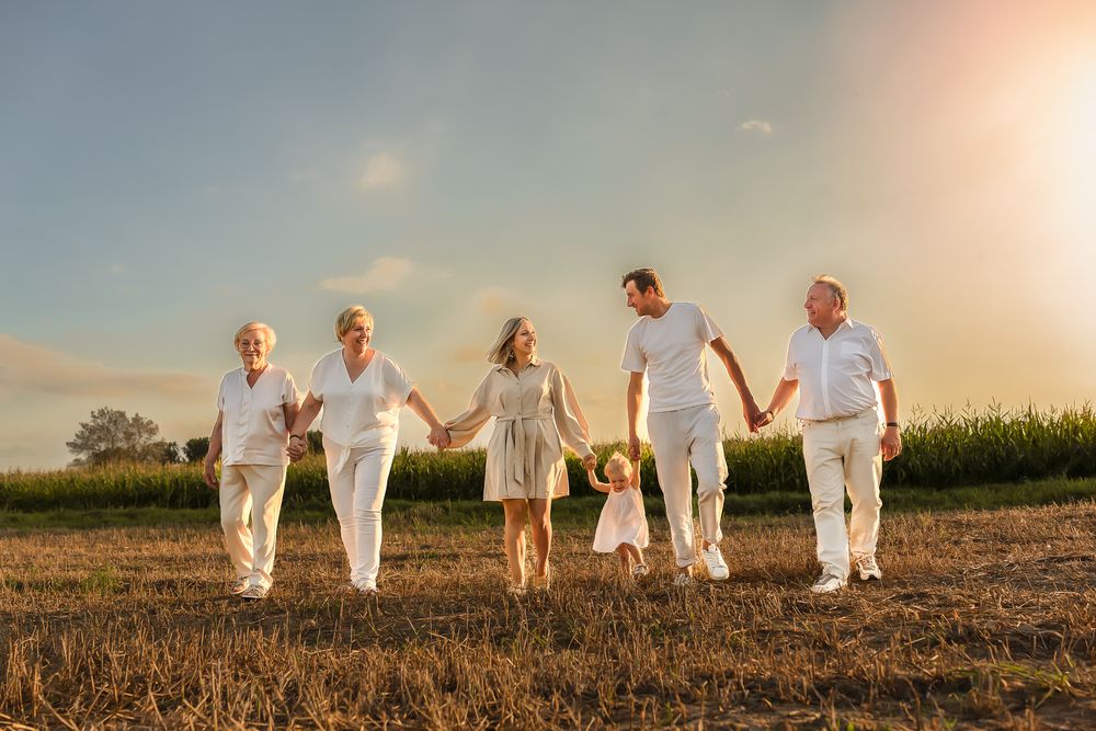 A group holds hands while walking through a golden-lit field at sunset wearing white.