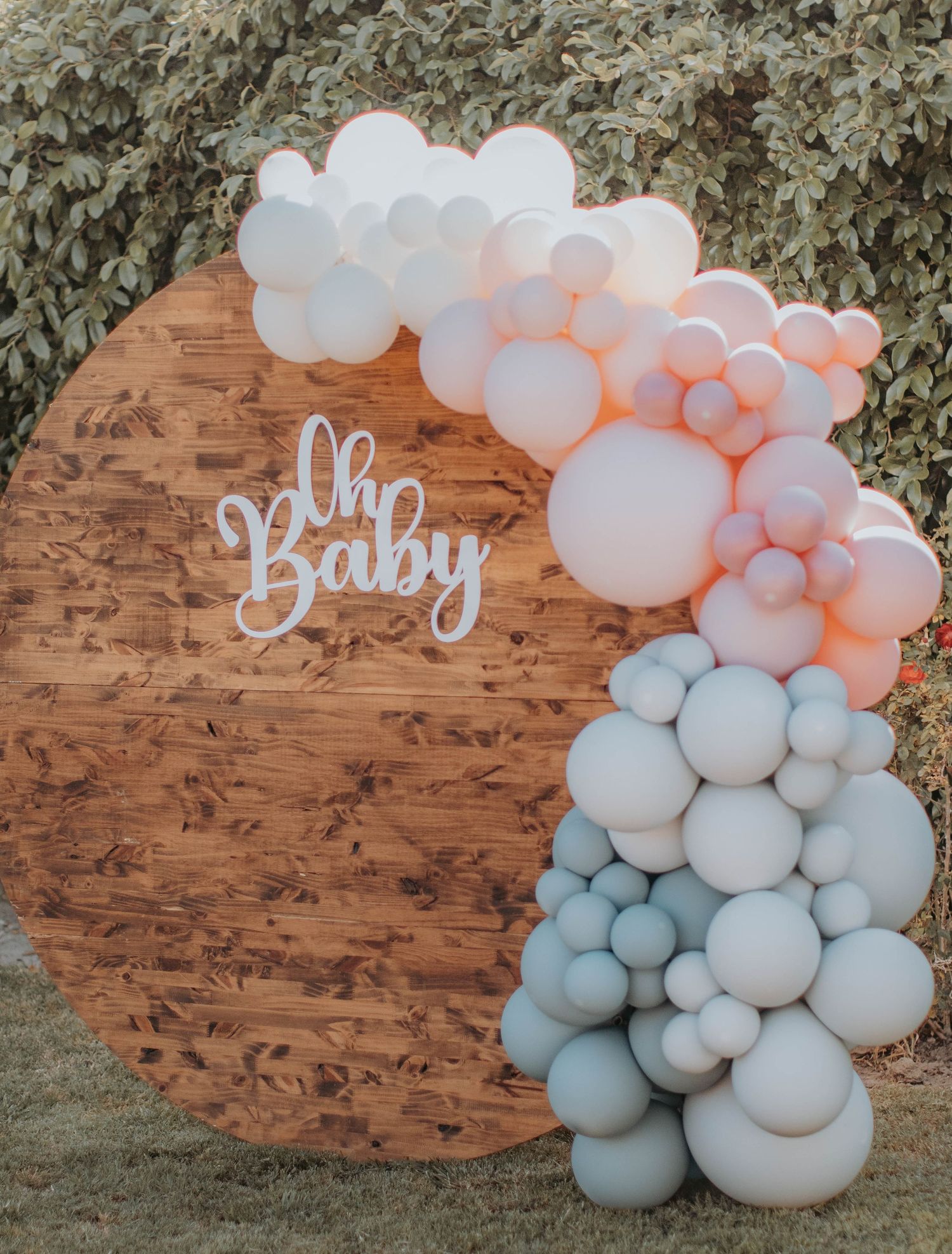 Baby shower decoration featuring pink and blue balloon arch against wooden backdrop.