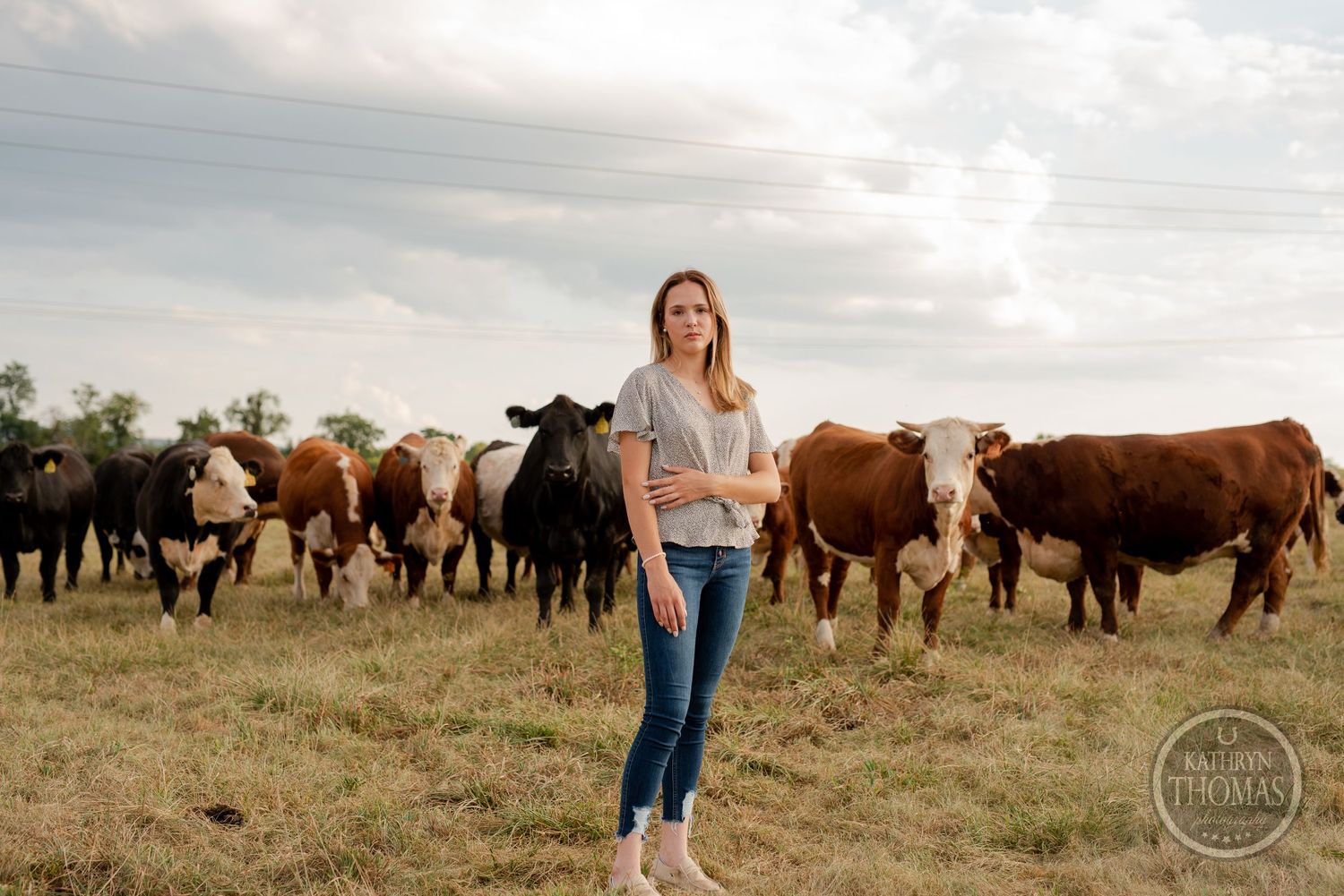 Casual outdoor portrait in pasture with diverse herd of cattle grazing behind.