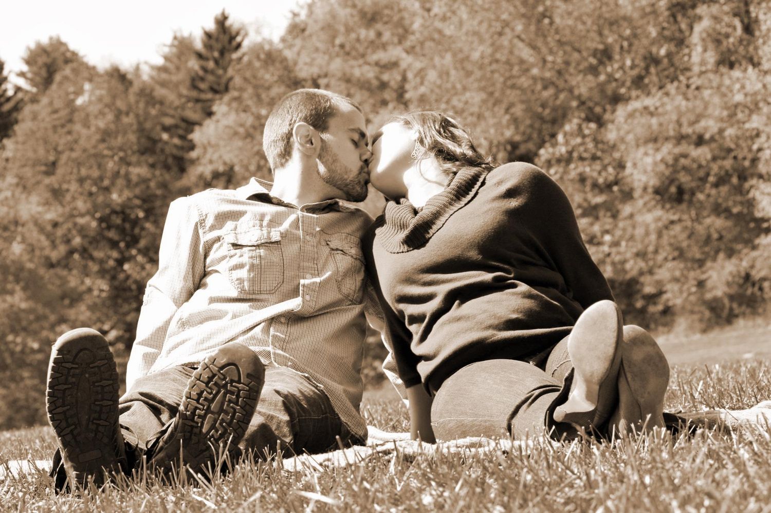 couple sitting on ground with legs extended forward. they lean together to kiss