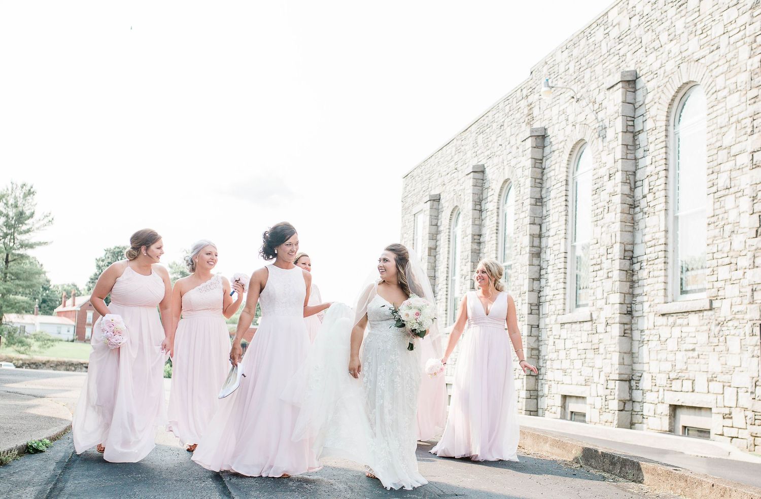 Group in pink and white dresses walking together outside stone building.