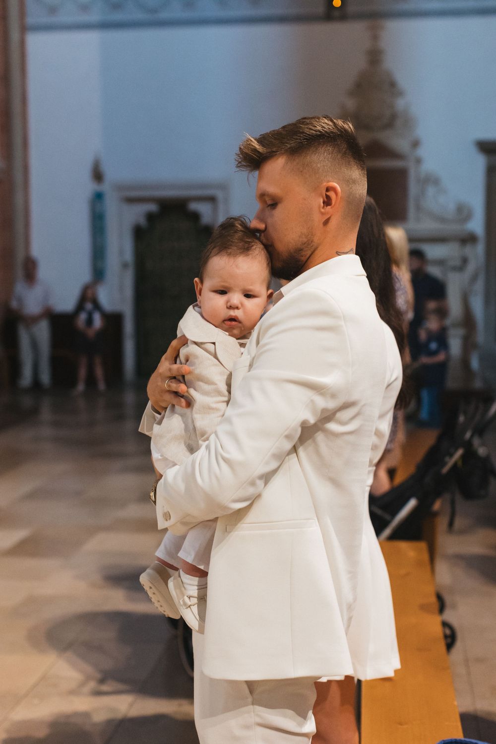 Father in white suit tenderly kissing baby in church christening ceremony.