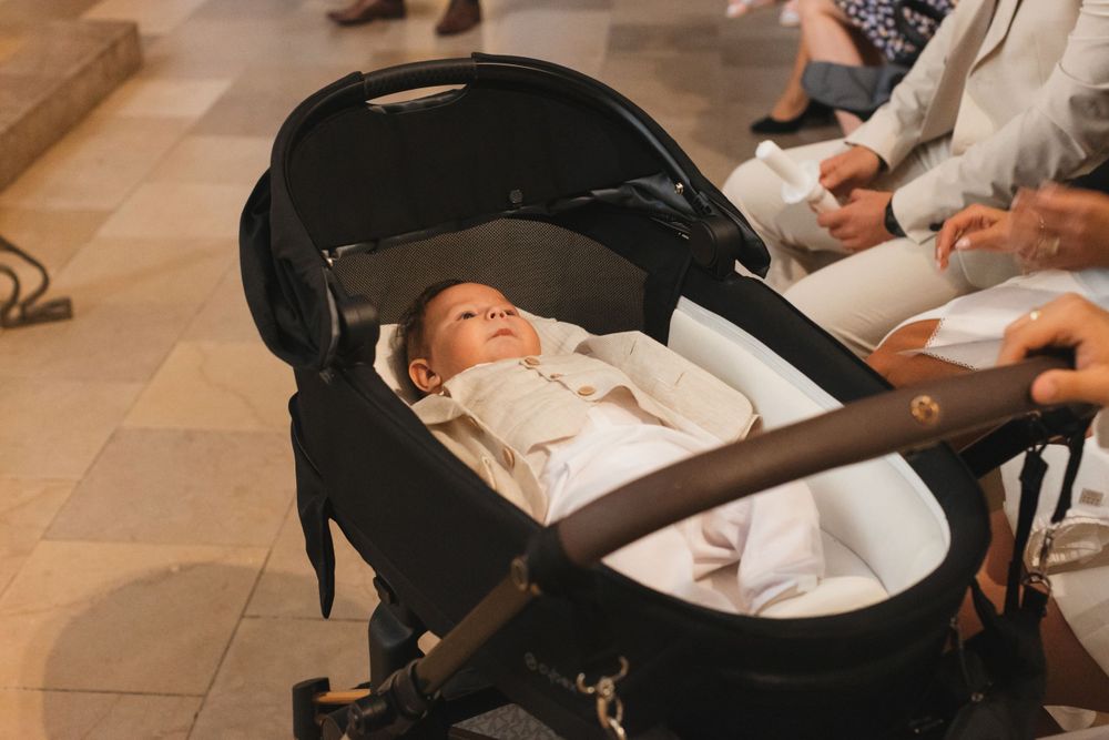Newborn baby in white outfit resting peacefully in black luxury pram.