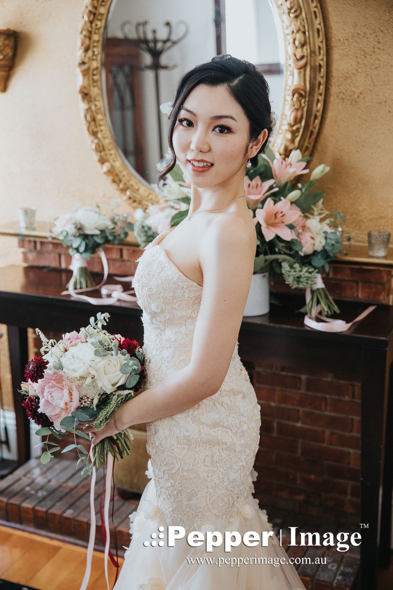 Smiling bride in a strapless mermaid lace gown holding a pink and white bridal bouquet.