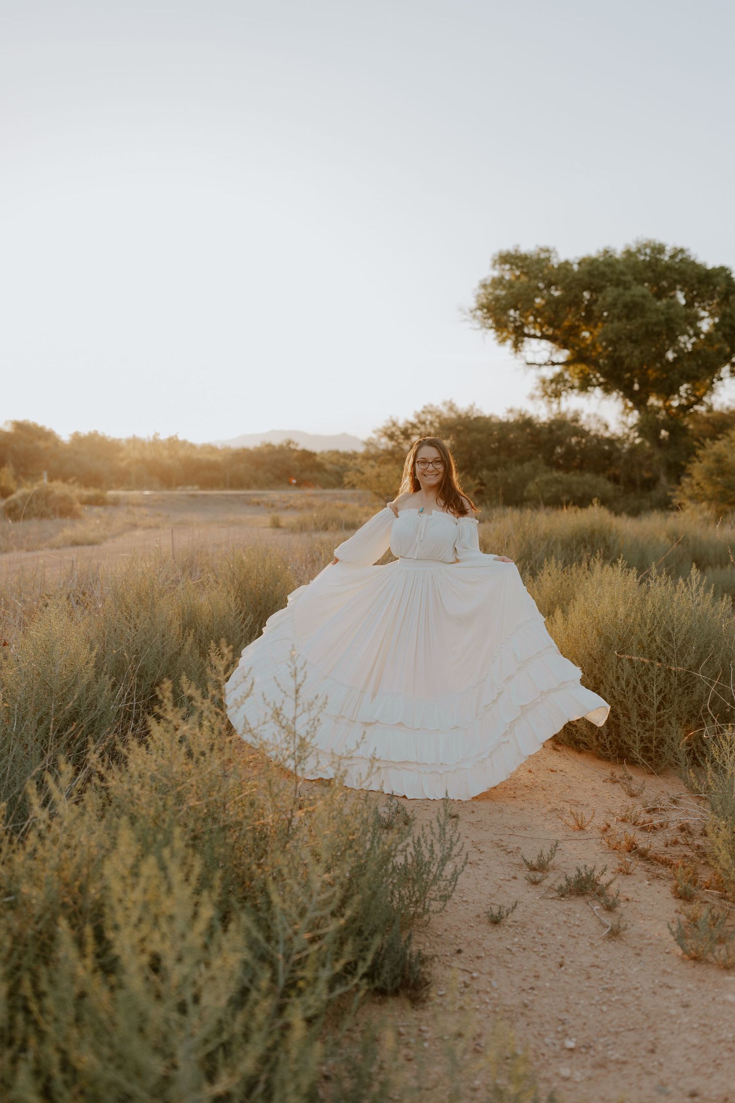 White dress flowing in motion against desert brush at sunset.