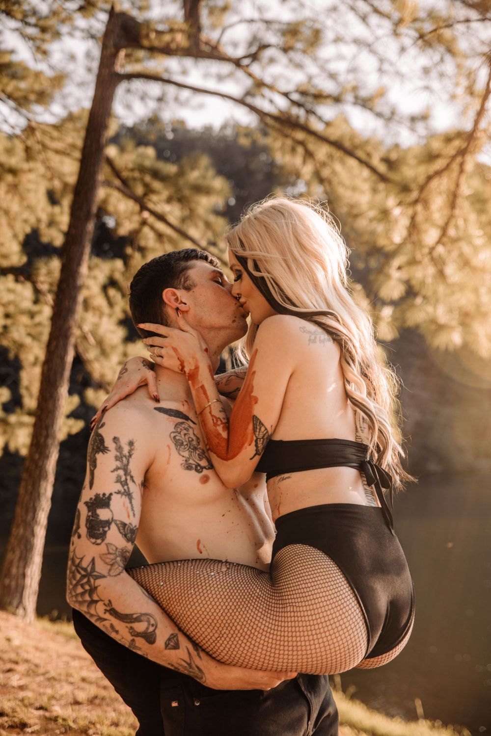 A couple embraces intimately in a sun-drenched forest setting with golden light filtering through the trees.