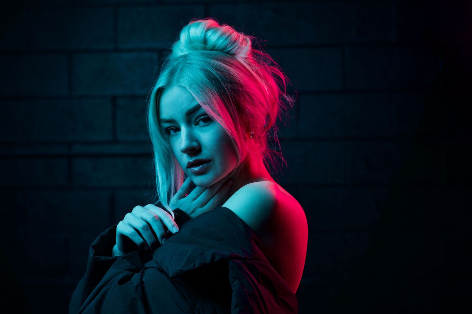 Dramatic portrait with neon red and blue lighting against a dark brick wall background.
