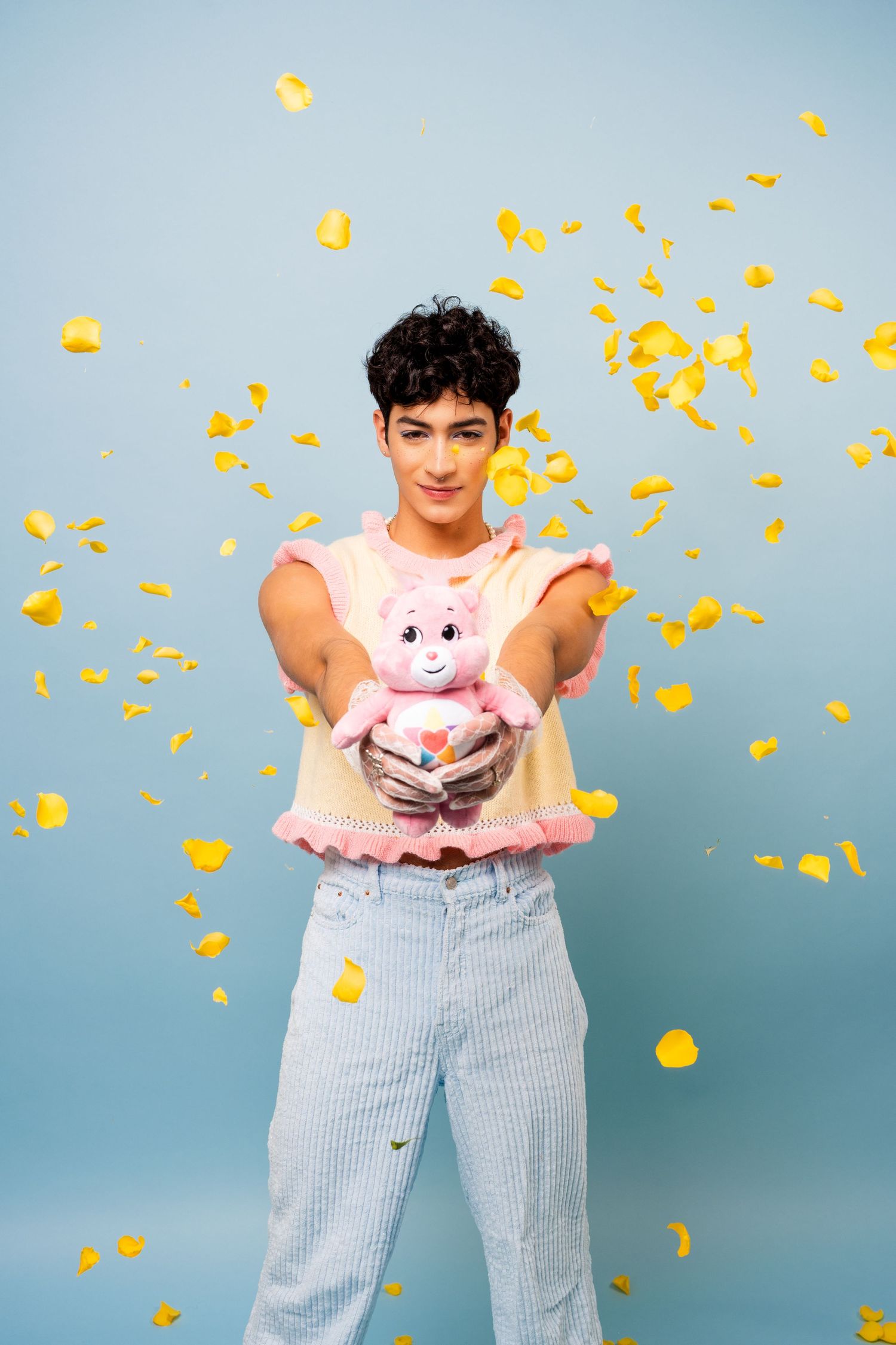 Playful scene with pink plush bear and falling yellow confetti against blue background.